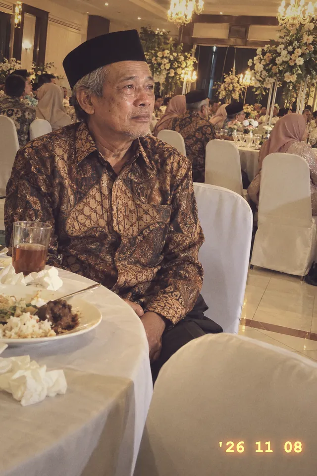 Ayah pengantin duduk di meja tamu menatap ke arah pelaminan